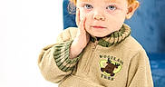 Jason is registered to the contest to win money with this photo: child, toddler, red_hair, blue_eyes, sweater, woodland_tree, hand_on_face, green_pants, indoor, portrait, cute, cozy_clothing, expression, curly_hair, seated, soft_lighting, furniture, white_background, casual, young_child