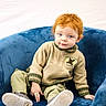 toddler, child, red_hair, blue_chair, cozy_clothing, sneakers, casual_wear, indoor, portrait, cute, seated, young_child, face, expression, light_background, plush_furniture, relaxed_pose, small_person, fashion, skin