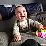 baby, smiling, toy, couch, child, happy, indoor, clothing, face, hand, infant, person, playful, colorful, young, portrait, cozy, cute, expression, warm