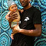 baby, child, man, person, smile, holding, crochet, hat, outdoor, nature, pattern, fabric, blue, green, shirt, black_clothing, happy, portrait, background, casual