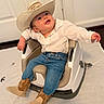 baby, cowboy_hat, boots, jeans, white_shirt, baby_seat, indoor, smiling, child, cute, happy, toddler, modern_furniture, floor, door, light, pose, portrait, clothing, infant