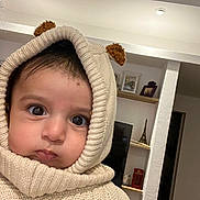 Omar a rejoint le concours — aidez-le/la à gagner de superbes lots ! baby, child, hoodie, knitwear, cream_color, face, big_eyes, indoors, living_room, shelf, decor, toy, portrait, cute, warm_clothing, person, headwear, expression, cozy, closeup