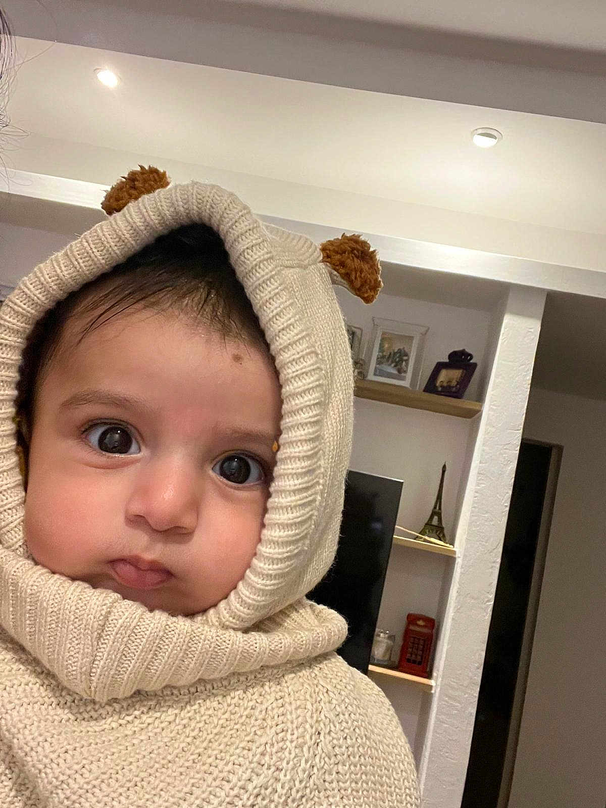 Omar a rejoint le concours — aidez-le/la à gagner de superbes lots ! baby, child, hoodie, knitwear, cream_color, face, big_eyes, indoors, living_room, shelf, decor, toy, portrait, cute, warm_clothing, person, headwear, expression, cozy, closeup