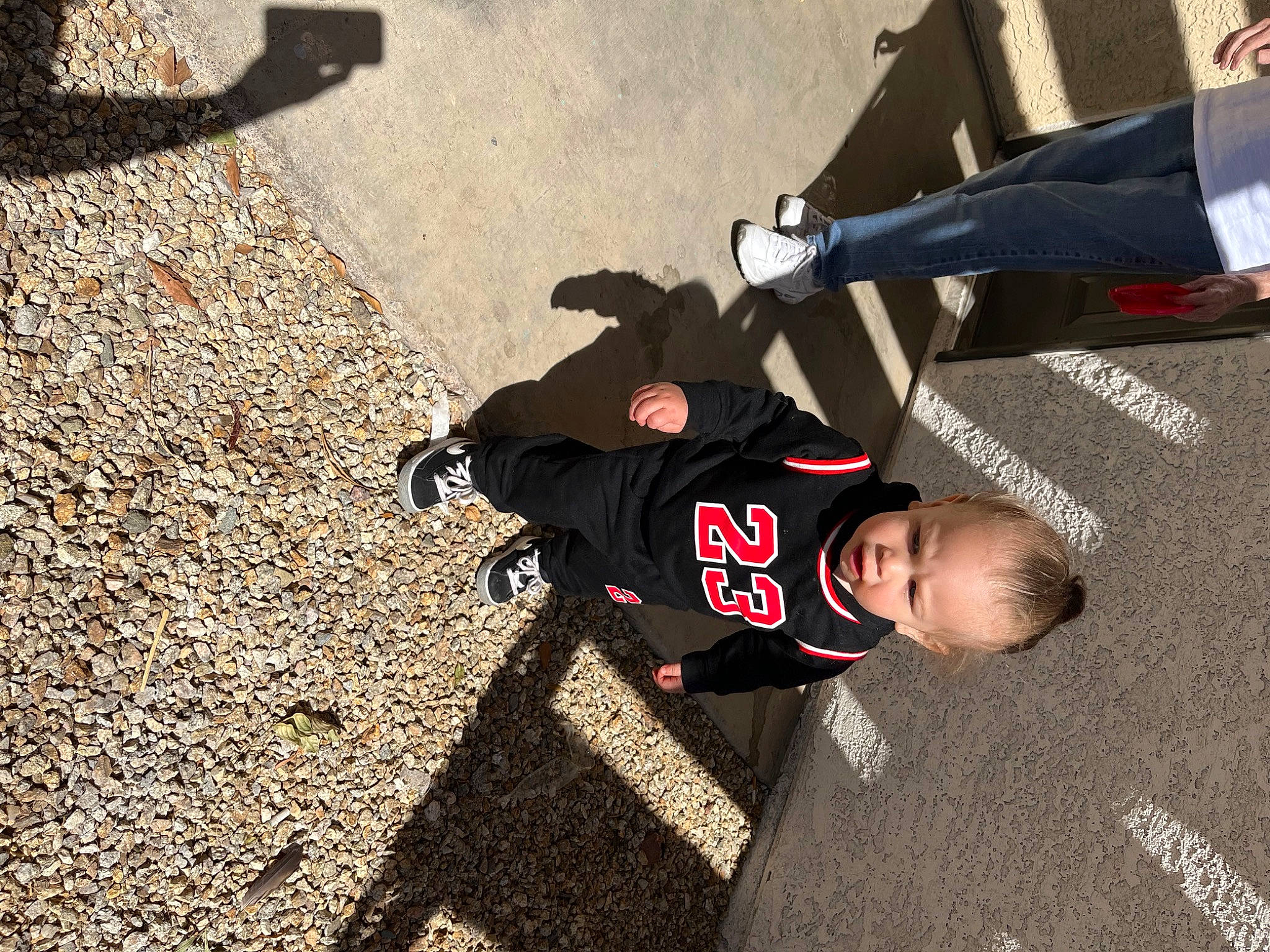 Malakai is registered to the contest to win money with this photo: asphalt, carmine, concrete, flooring, font, fun, outdoor_shoe, pedestrian, person, recreation, road, road_surface, shadow, shoe, sidewalk, sitting, sneakers, street, tar, toddler