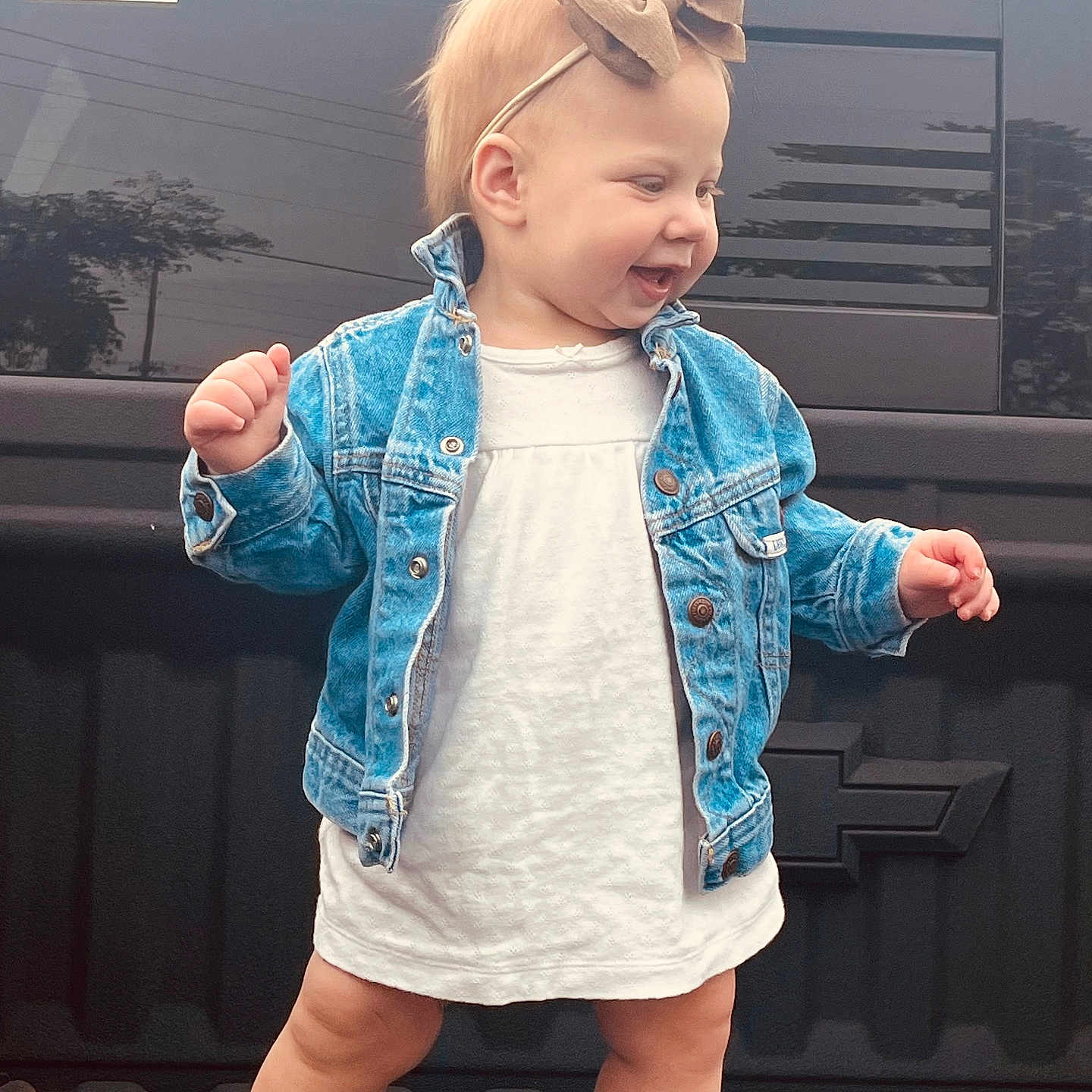 Joella joined the competition — help win amazing prizes! american_flag_sticker, baby, bow_headband, casual_clothing, chevrolet_logo, child, cute, daytime, denim_jacket, footwear, happy, legs, outdoor, pickup_truck, portrait, smiling, standing, toddler, vehicle, white_dress