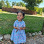 child, girl, smiling, outdoor, dress, keys, fence, grass, tree, rocks, sunny, happy, footwear, sandals, curly_hair, playful, nature, daylight, portrait, cute