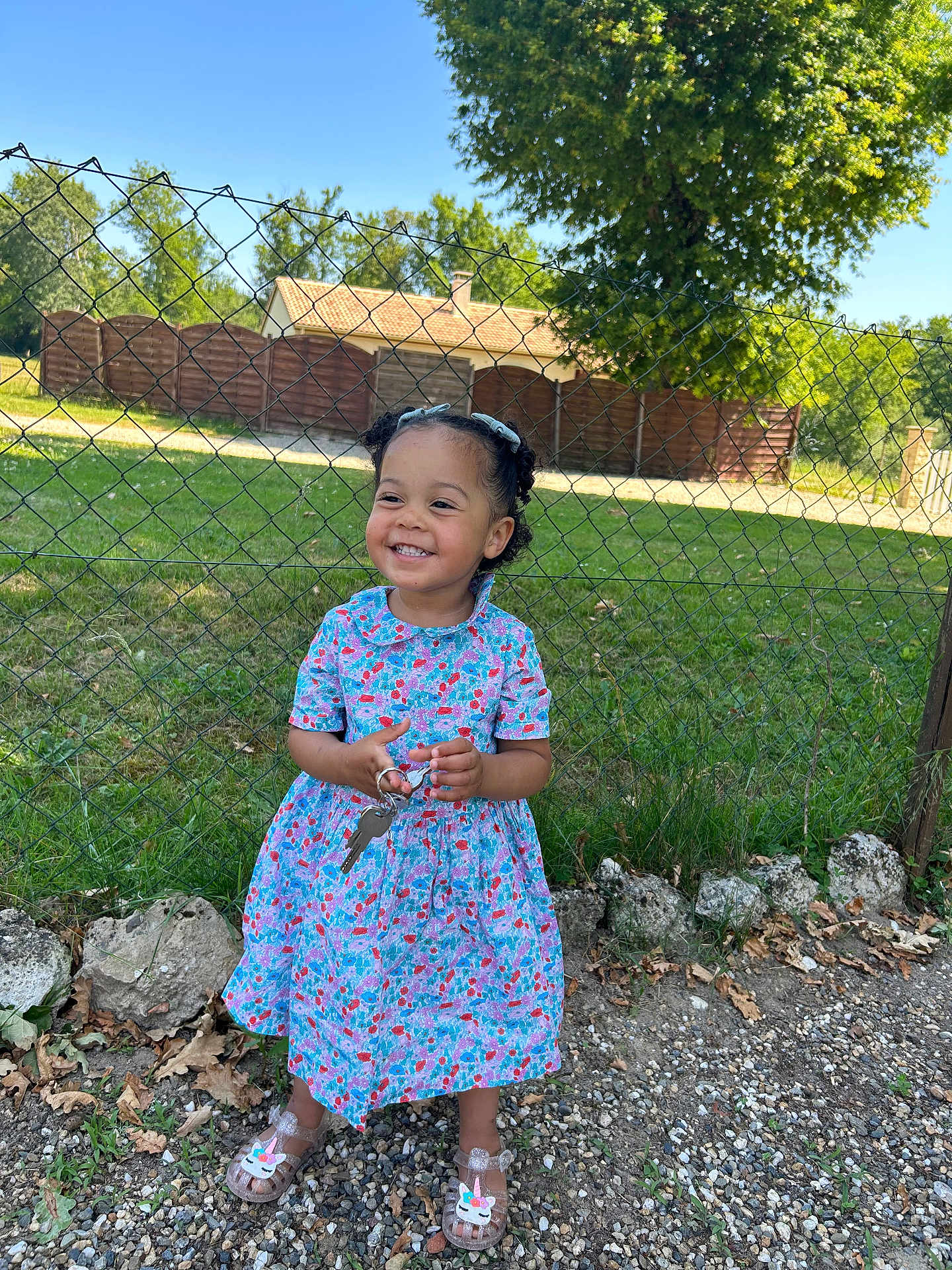 Lena a rejoint le concours — aidez-le/la à gagner de superbes lots ! child, girl, smiling, outdoor, dress, keys, fence, grass, tree, rocks, sunny, happy, footwear, sandals, curly_hair, playful, nature, daylight, portrait, cute