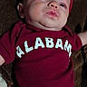 baby, bow, casual, child, closeup, curious, cute, expression, fabric, face, headwear, indoors, infant, lying_down, maroon_clothing, person, portrait, pouty, soft_lighting, young
