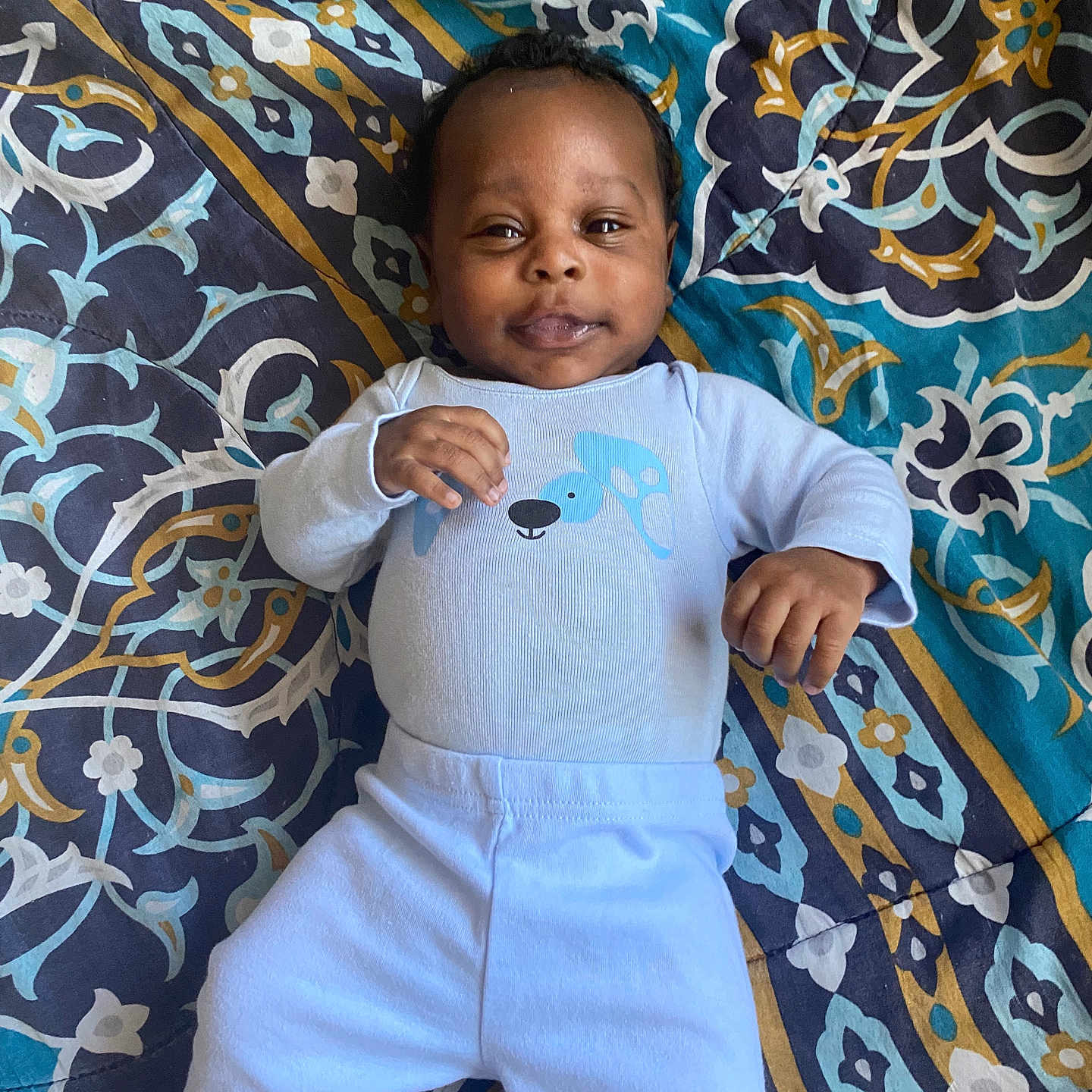 Dakari is registered to the contest to win money with this photo: baby, babylaughing, bodypart, clothing, cushion, face, finger, hand, happy, head, homedecor, pants, person, photography, portrait, quilt, sitting, sleeve, smile, standing