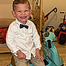 Ayden a rejoint le concours — aidez-le/la à gagner de superbes lots ! child, boy, smiling, toy_scooter, indoor, white_shirt, bow_tie, khaki_pants, socks, shoes, wooden_floor, stuffed_animal, bed, playroom, toy, furniture, happy, portrait, person, floor_mat