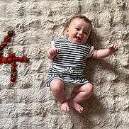 Louise a rejoint le concours — aidez-le/la à gagner de superbes lots ! baby, barefoot, celebration, child, cute, fluffy_rug, fruit, happy, indoors, infant, lying_down, number_four, playful, portrait, skin, smiling, soft_texture, strawberries, striped_clothing, young