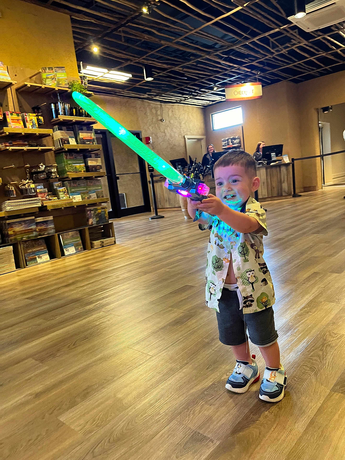 Asher joined the competition — help win amazing prizes! child, toy, sword, glowing, indoor, store, floor, wooden_floor, shelf, books, games, shorts, shirt, sneakers, happy, smiling, person, play, light, ceiling