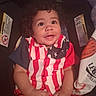 baby, child, curly_hair, car_seat, smiling, shirt, red, white, blue, stars, stripes, cute, portrait, indoors, happy, infant, clothing, person, seat_belt, sitting