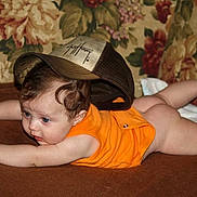 Autumn joined the competition — help win amazing prizes! baby, infant, child, blue_eyes, curly_hair, orange_onesie, cap, hat, tummy_time, crawling, couch, floral_wallpaper, blanket, brown_surface, indoor, portrait, curious_expression, bare_legs, plush_fabric, young_child