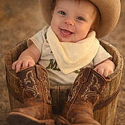 Noah Steven joined the competition — help win amazing prizes! baby, infant, smile, cowboy_hat, cowboy_boots, wooden_bucket, bandana, portrait, outdoor, rustic, cute, hands, eyes, sitting, bokeh, shallow_depth_of_field, clothing, hat, footwear, warm_tones