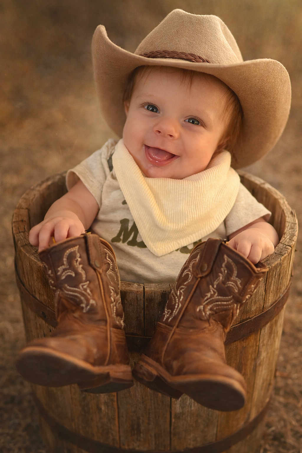 Noah Steven joined the competition — help win amazing prizes! baby, infant, smile, cowboy_hat, cowboy_boots, wooden_bucket, bandana, portrait, outdoor, rustic, cute, hands, eyes, sitting, bokeh, shallow_depth_of_field, clothing, hat, footwear, warm_tones