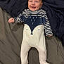 baby, infant, smiling, onesie, animal_print, striped_clothing, bed, blanket, happy, cute, face, person, child, footed_pajamas, lying_down, indoors, soft_lighting, comfort, cozy, portrait