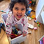child, toddler, smiling, curly_hair, toy_box, toys, indoor, hardwood_floor, pajamas, minnie_mouse, laughing, excited, face, hands, playroom, storage_box, colorful, floor, bucket, portrait
