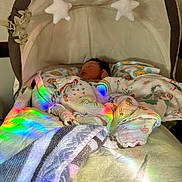 Lucian is registered to the contest to win money with this photo: baby, sleeping, bassinet, blanket, stars, soft_toys, rainbow_light, cozy, indoor, child, infant, nursery, fabric, toddler, cute, peaceful, sleep, colorful, pattern, resting