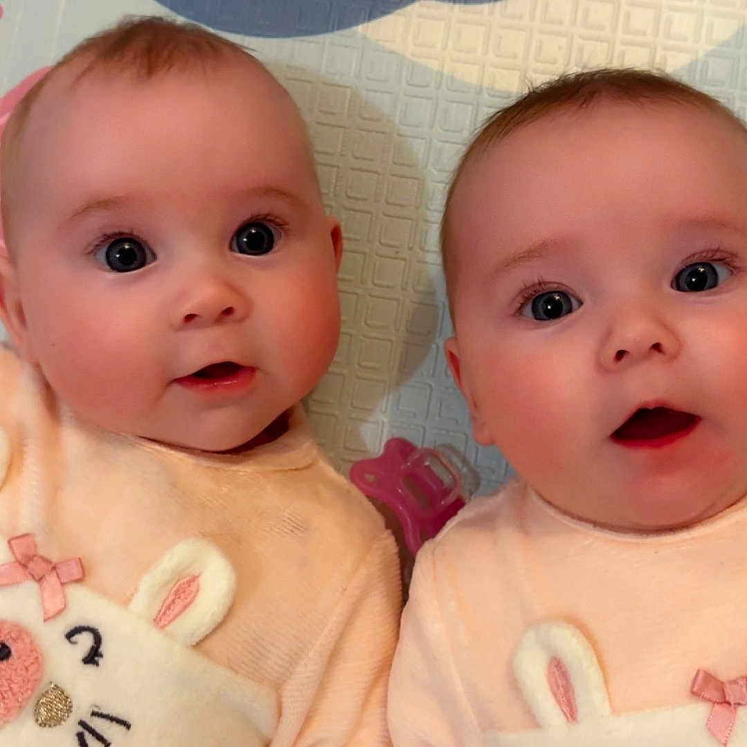 Romy Et Léna a rejoint le concours — aidez-le/la à gagner de superbes lots ! adorable, baby, bunny_design, child, closeup, cute, expression, face, indoor, infant, lying_down, matching_clothes, pastel_colors, peach_outfit, pink_seahorse, play_mat, soft_lighting, twin, two_babies, wide_eyes
