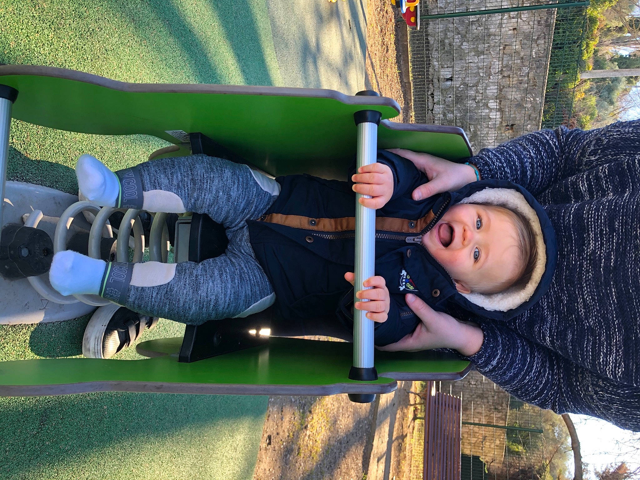 Enzo participe au concours pour gagner de l'argent avec cette photo : baby_products, child, city, electric_blue, fun, grass, jacket, knee, leisure, outdoor_play_equipment, person, playground, product, public_space, recreation, sitting, swing, toddler, tree