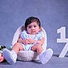 baby, background, calm_expression, child, clothing, cozy_chair, cute, decor, flowers, half_year, indoor, infant, milestone, person, pink_flowers, portrait, sitting, studio, white_flowers, white_shoes