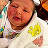 newborn, baby, infant, child, face, portrait, eyes, mouth, smiling, blanket, swaddled, cartoon, colorful, indoors, close_up, person, arms, tattoo, crib, cozy