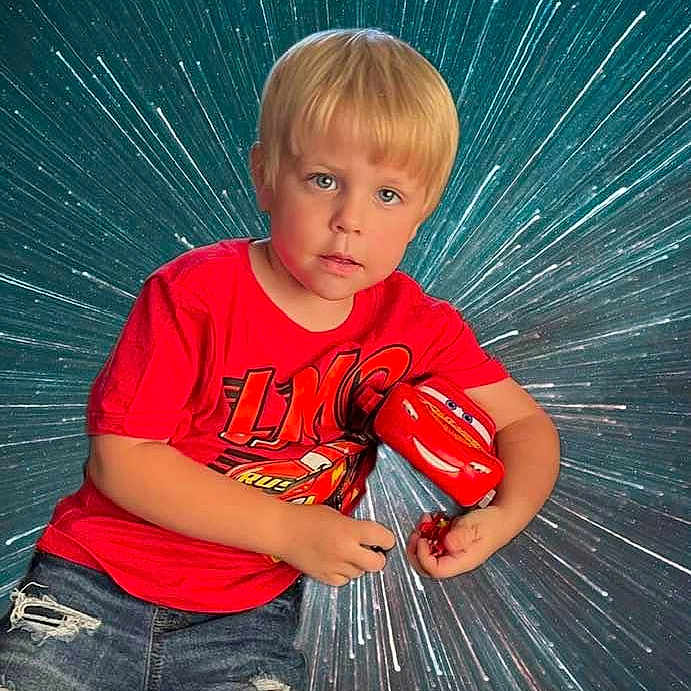 Jordan is registered to the contest to win money with this photo: blond_hair, boy, cars_movie, casual_clothing, child, cute, dynamic_background, indoor, jeans, lightning_mcqueen, photography, playful, portrait, posing, red_shirt, smiling, starburst, studio_background, toy, young_child