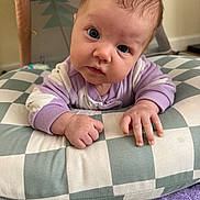 Kaia joined the competition — help win amazing prizes! baby, infant, face, curious, pillow, checkered, purple, white, blanket, hand, indoors, cute, child, young, soft, clothing, portrait, lying_down, expression, head