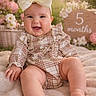 baby, blanket, bow, child, chubby_cheeks, cute, flowers, happy, headband, indoor, infant, milestone_sign, person, plaid_clothing, portrait, sitting, skin, smiling, soft_lighting, wooden_sign