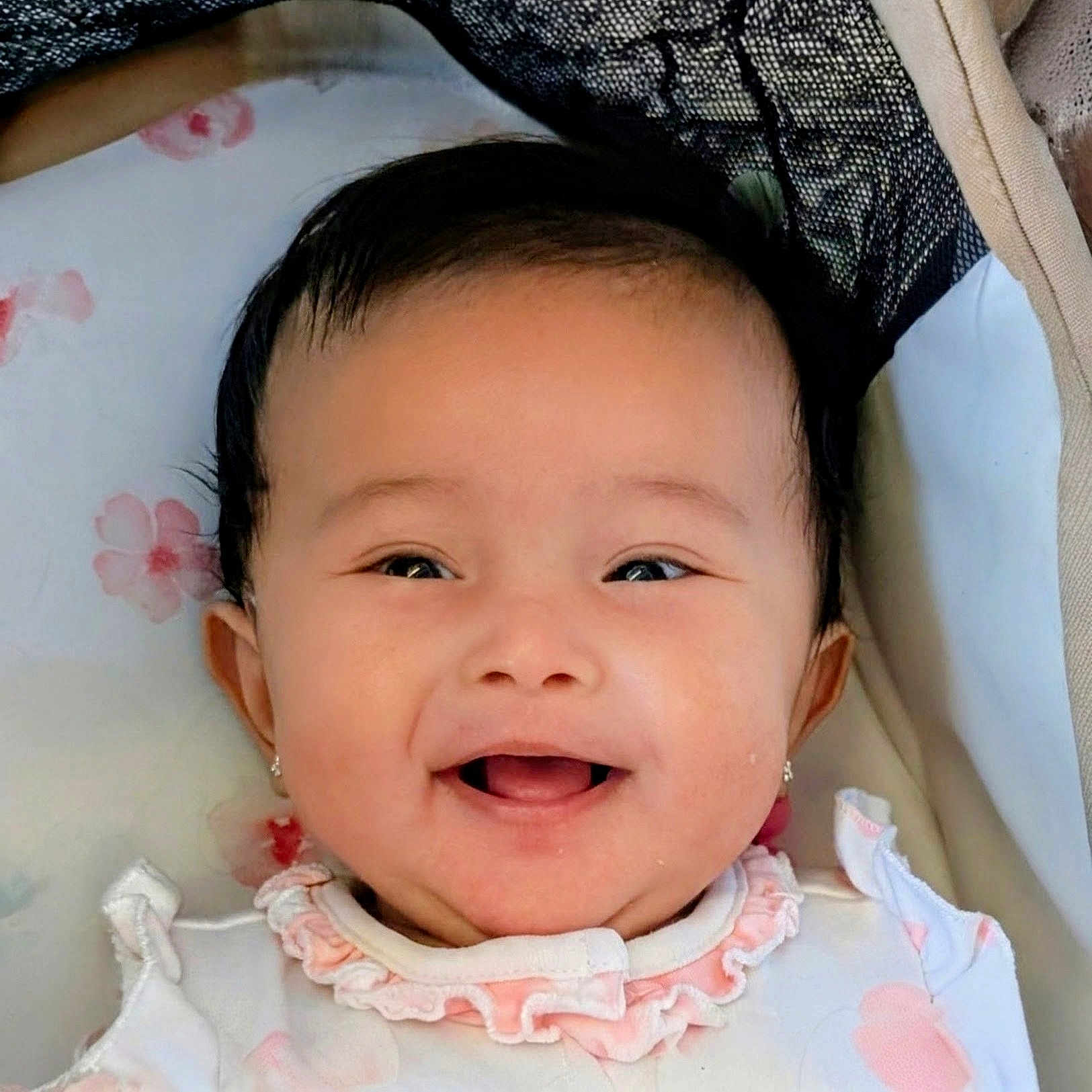 Madison joined the competition — help win amazing prizes! baby, infant, child, smiling, happy, portrait, face, close_up, eyes, mouth, black_hair, floral, blanket, cradle, bedding, pink_clothing, white_clothing, indoors, sitting, photography