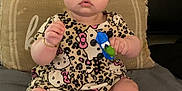 Olivia Jeanmarie is registered to the contest to win money with this photo: baby, child, toy, plush_toy, unicorn, dress, patterned_clothing, silver_shoes, bed, pillow, headboard, indoor, sitting, wide_eyed, curious, bracelet, infant, person, cute, expression