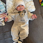 Noah a rejoint le concours — aidez-le/la à gagner de superbes lots ! baby, infant, mickey_mouse, onesie, hat, cushion, couch, sneakers, smile, face, clothing, blanket, indoor, cute, child, person, footwear, soft_texture, relaxing, happy