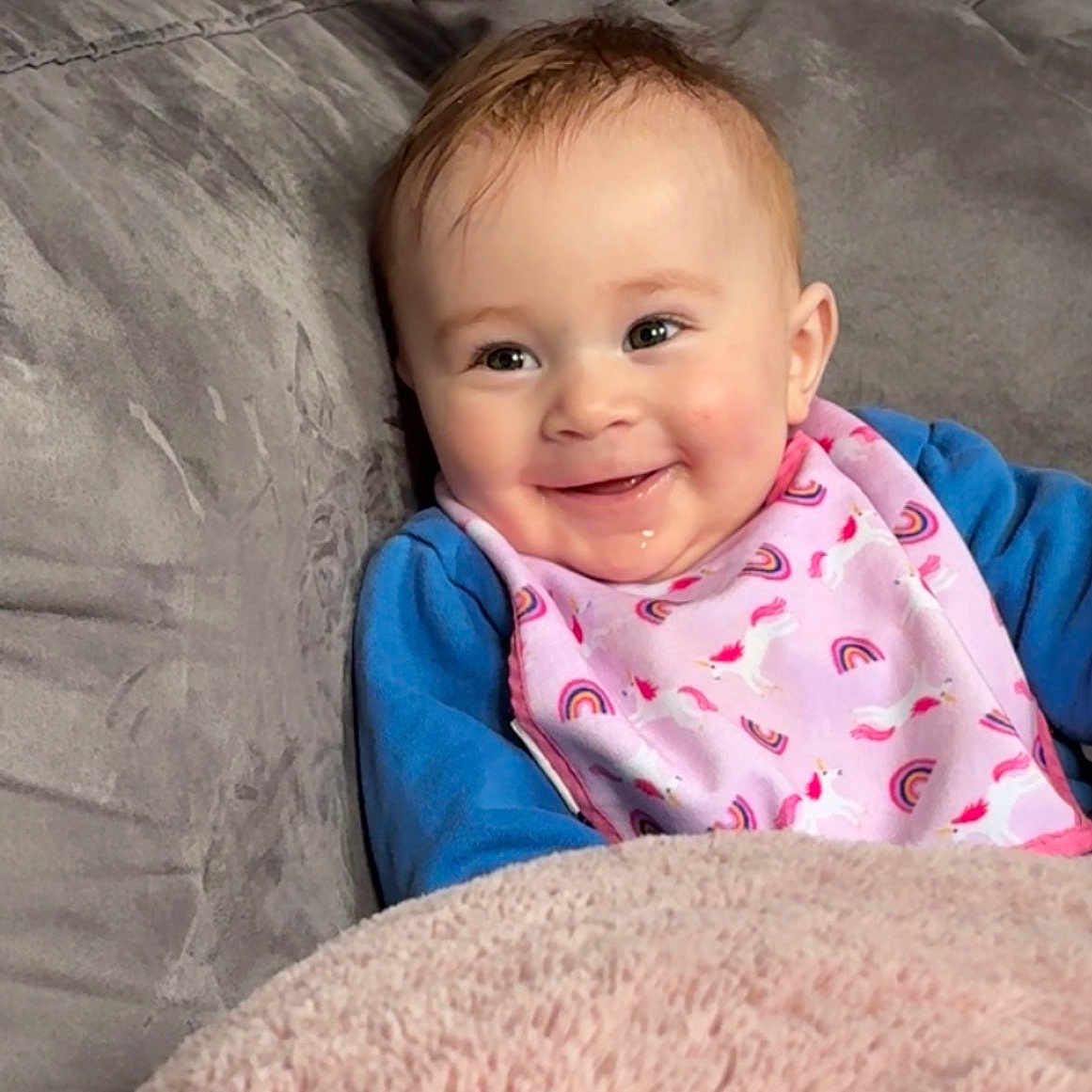 Noah participe au concours pour gagner de l'argent avec cette photo : baby, smiling, bib, unicorn, rainbow, pink, blue_clothing, blanket, couch, face, child, indoors, cozy, happy, person, infant, seated, soft_texture, home, cute