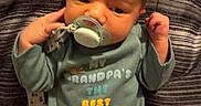 Oliver joined the competition — help win amazing prizes! baby, infant, pacifier, onesie, clothing, striped_blanket, lying_down, hand, face, head, cute, newborn, child, indoors, text_on_clothing, raised_fist, blanket, soft_fabric, portrait, young_child