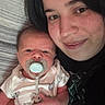 Oliver is registered to the contest to win money with this photo: baby, newborn, pacifier, woman, smile, face, portrait, indoor, bed, striped_bedspread, holding, caring, family, love, comfort, clothing, person, skin, head, hair