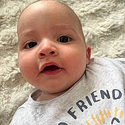 Aymen a rejoint le concours — aidez-le/la à gagner de superbes lots ! baby, infant, face, closeup, expression, eyes, mouth, skin, head, clothing, tshirt, text, sun, blanket, soft, cute, young, portrait, lying, indoors