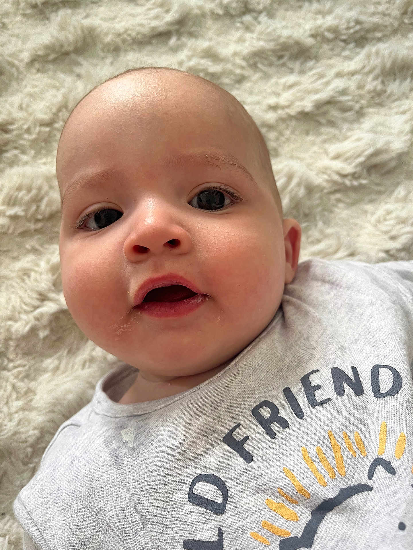 Aymen a rejoint le concours — aidez-le/la à gagner de superbes lots ! baby, infant, face, closeup, expression, eyes, mouth, skin, head, clothing, tshirt, text, sun, blanket, soft, cute, young, portrait, lying, indoors