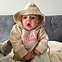 baby, hoodie, child, person, clothing, beige, indoor, couch, blanket, expression, surprised, cute, casual, sitting, warm, portrait, face, hands, soft, young