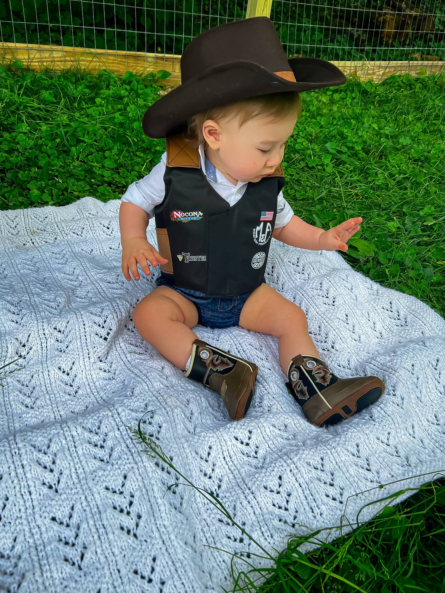 Bruce is registered to the contest to win money with this photo: baby_toddler_clothing, cap, fun, grass, happy, hat, human_leg, lawn, leaf, leg, leisure, people_in_nature, person, plant, recreation, shorts, sitting, sleeve, sun_hat, thigh