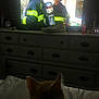 cat, television, firefighter, dresser, shoes, bottle, clock, bed, dark, indoor, screen, watching, furniture, reflection, person, helmet, fire_suit, oxygen_tank, blur, shadow