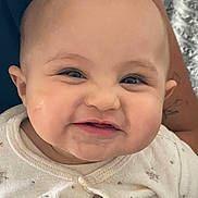 Jessey participe au concours pour gagner de l'argent avec cette photo : baby, smile, face, chubby_cheeks, infant, close_up, white_clothing, patterned_outfit, skin, person, portrait, young_child, cute, happy, expression, tattoo, adult_arm, holding, indoor, soft_texture