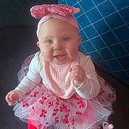 Lainey is registered to the contest to win money with this photo: baby, child, smiling, pink, headband, bow, tutu, tulle, red, leggings, pacifier, sitting, couch, blue_cushion, happy, indoors, cute, portrait, infant, clothing