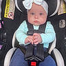 apparel, baby, blue_eyes, bow, car_seat, child, child_seat, clothing, cute, face, hands, headband, indoor, infant, person, portrait, safety, seatbelt, sitting, young_child