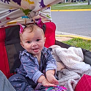 Arabella joined the competition — help win amazing prizes! baby, child, tongue_out, wagon, blanket, toy_phone, hair_accessory, outdoor, playful, cute, pink, red, smiling, clothing, grass, sidewalk, person, infant, seat, toy
