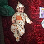 baby, infant, smiling, pumpkin_onesie, hat, red_rug, stuffed_animal, plush_toy, baby_wipes, happy, lying_down, cute, child, carpet, indoor, clothing, face, headwear, person, toddler