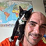 man, cat, shoulder, orange_shirt, black_and_white_cat, smile, bald, indoor, world_map, wall, green_collar, pet, happy, portrait, closeup, animal, friendship, feline, human, casual