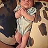 baby, infant, pillow, cow_print, sleepy, hands, legs, feet, clothing, onesie, skin, relaxing, resting, indoors, cushion, pattern, person, newborn, comfort, soft