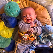 Milo is registered to the contest to win money with this photo: baby, smiling, stuffed_animal, plush_toy, play_mat, child, happy, infant, clothing, toddler, cute, soft_toy, indoors, colorful, cozy, face, person, blanket, socks, relaxing