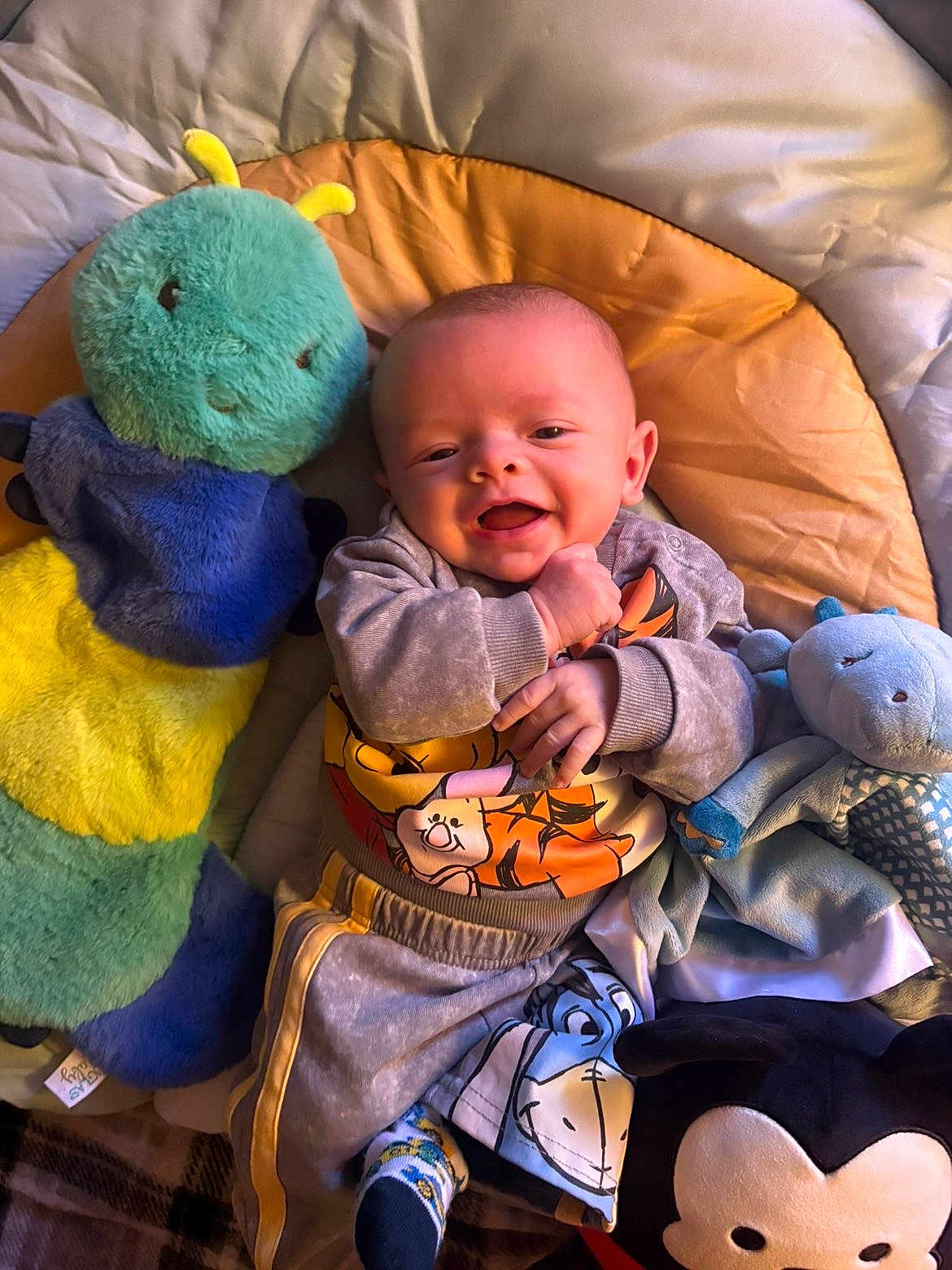 Milo is registered to the contest to win money with this photo: baby, smiling, stuffed_animal, plush_toy, play_mat, child, happy, infant, clothing, toddler, cute, soft_toy, indoors, colorful, cozy, face, person, blanket, socks, relaxing